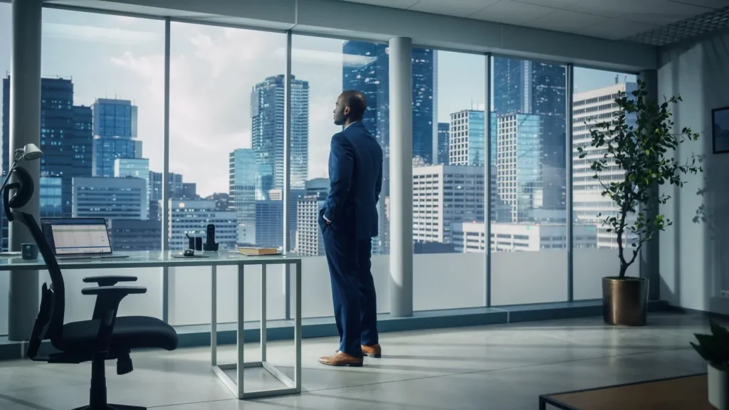 Nachdenklicher Mann steht im Business-Anzug in seinem Büro mit Blick auf die Skyline