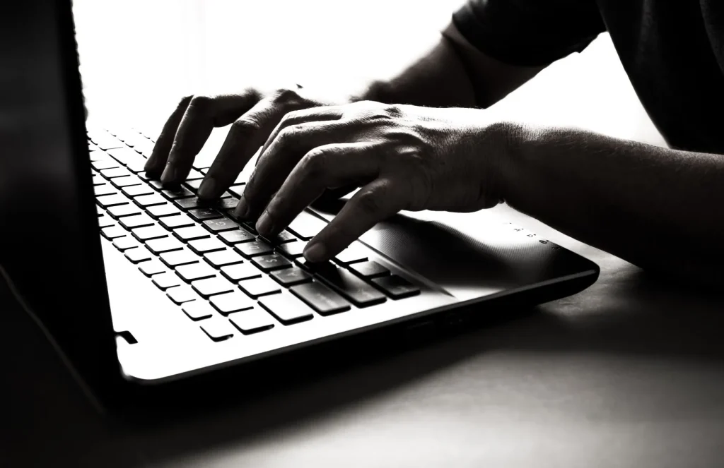 Schwarz-Weiß-Foto von einer Laptop-Tastatur und Fingern, die darauf tippen