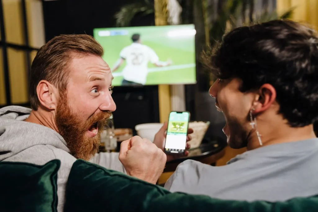 Zwei Männer jubeln beim Fußballgucken, weil sie mit Sportwetten Geld verdienen