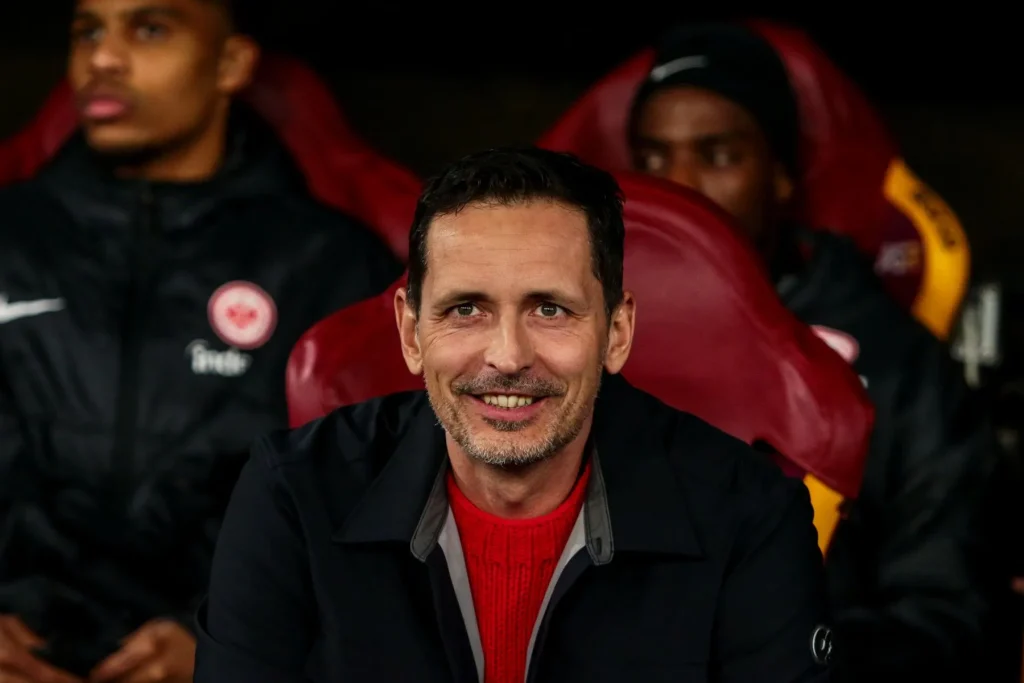 Dino Toppmöller, auf den die Quoten bei Trainerentlassung Wetten hoch sind, sitzt mit einem Lächeln auf der Trainerbank von Eintracht Frankfurt