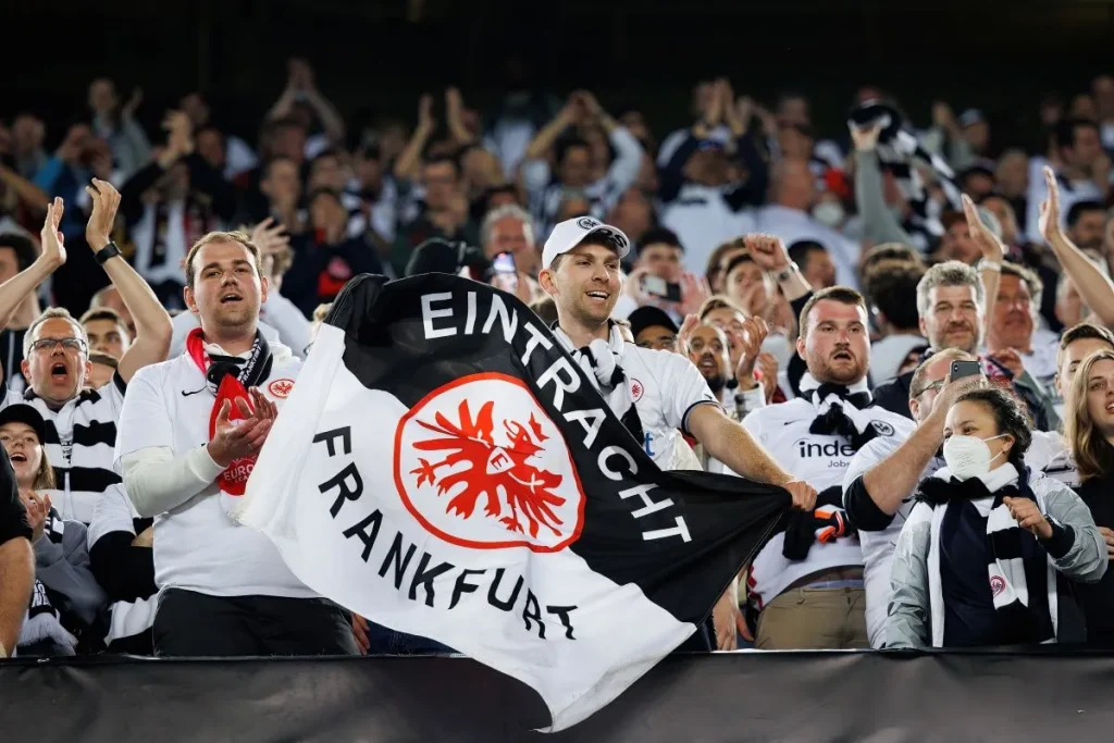 Fans von Eintracht Frankfurt, einem Mitfavoriten bei Deutscher Meister Wetten, jubeln im Stadion und halten eine Frankfurt-Fahne hoch